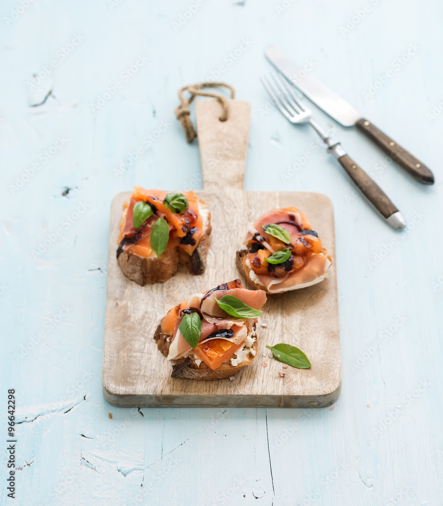 Bruschettas with Prosciutto，烤甜瓜，软奶酪和罗勒，放在木制服务板上，光线充足