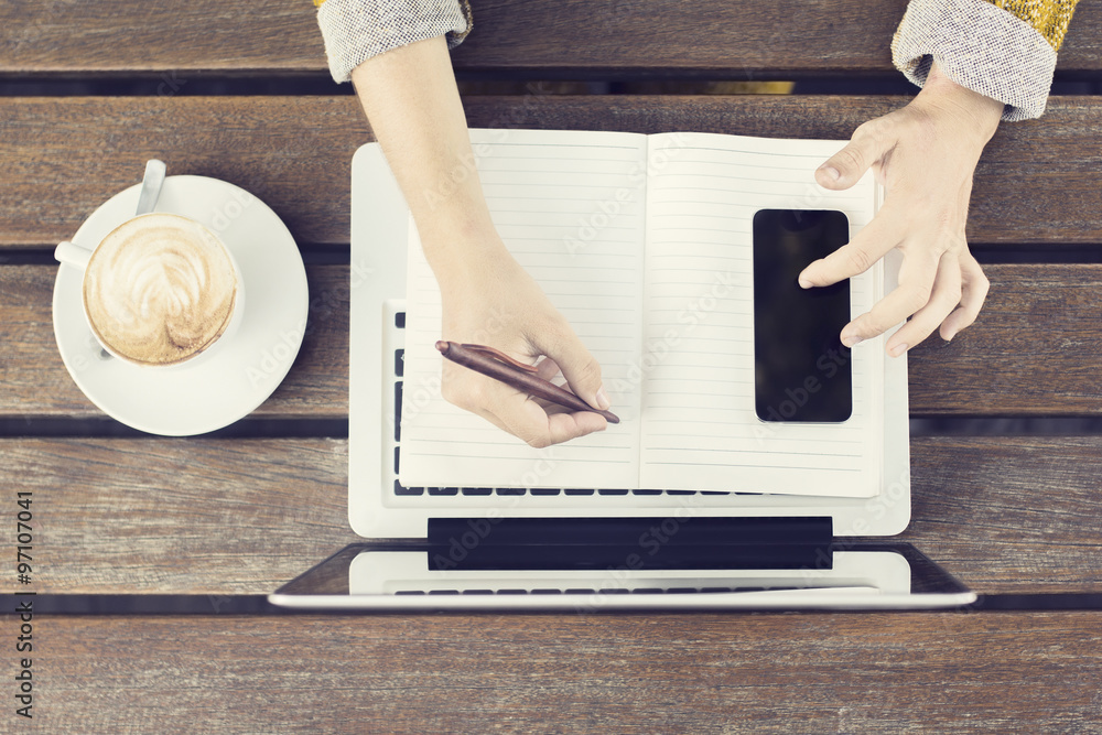 Girl with laptop, blank diary, cell phone and coffee mug on wood