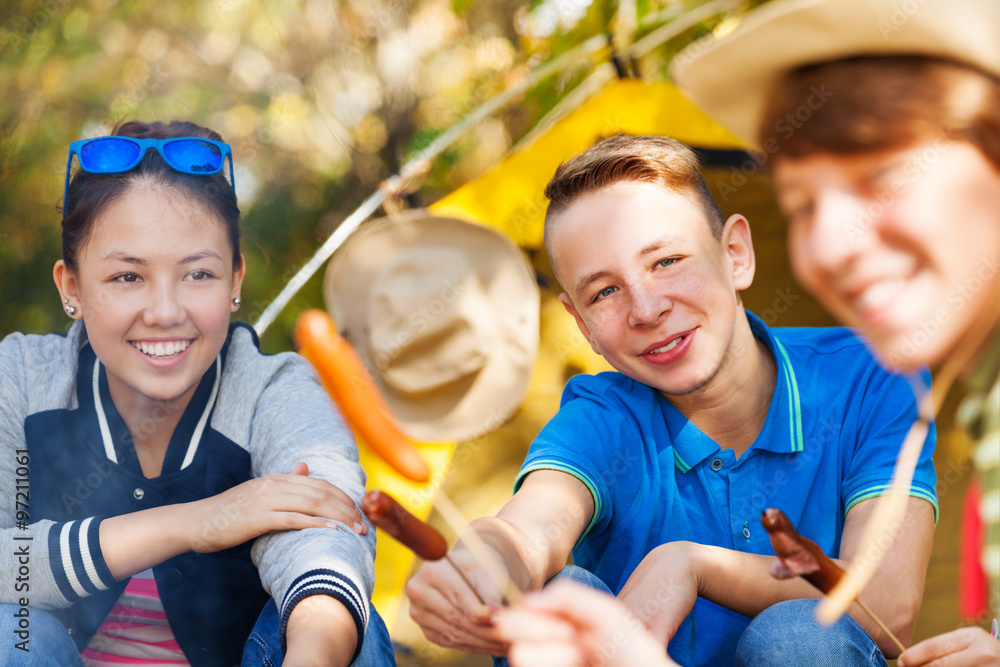 Teens hold sausages on sticks near fireplace