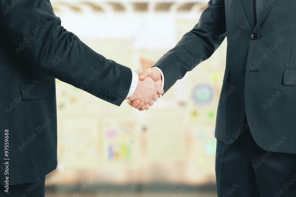 Business partners shake hands in the office at posters backgroun