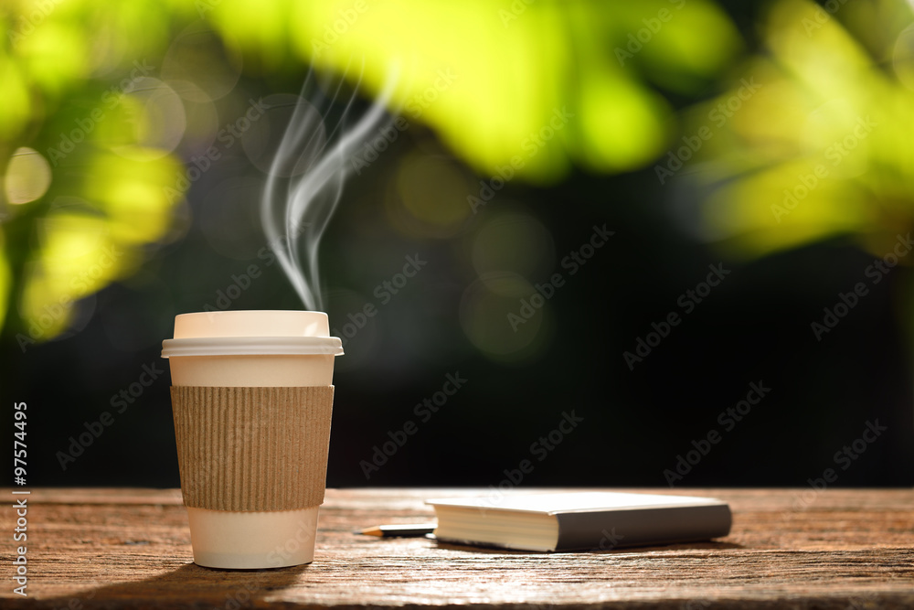 Paper cup of coffee with smoke and book in the garden