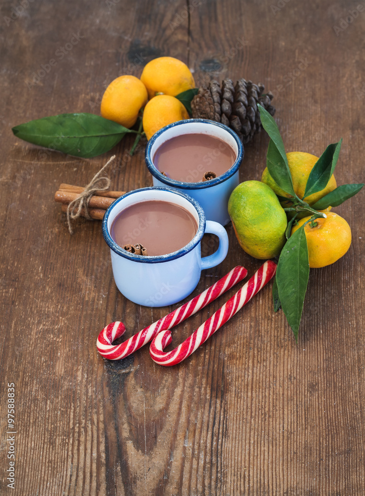 Hot chocolate in enamel metal mugs, fresh mandarins, cinnamon sticks, pine cone and candy canes over