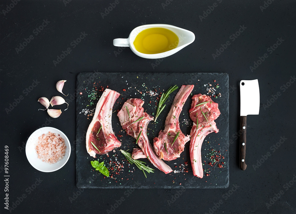 Raw lamb chops. Rack of Lamb with garlic, rosemary and spices on black slate tray, oil in a saucer, 