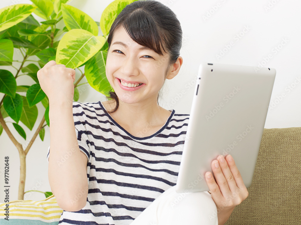 部屋でタブレットを使う女性　ガッツポーズ