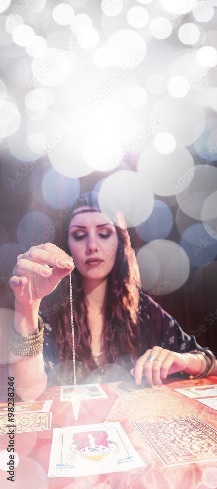 Composite image of female fortune teller using pendulum