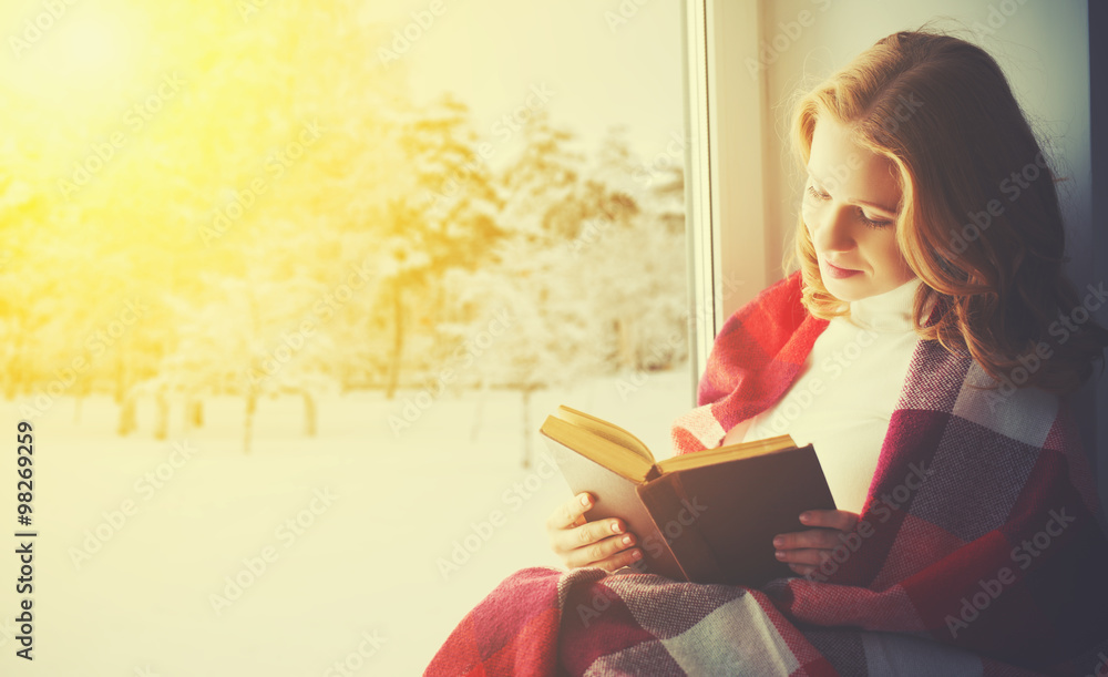 happy girl reading book by the window in winter