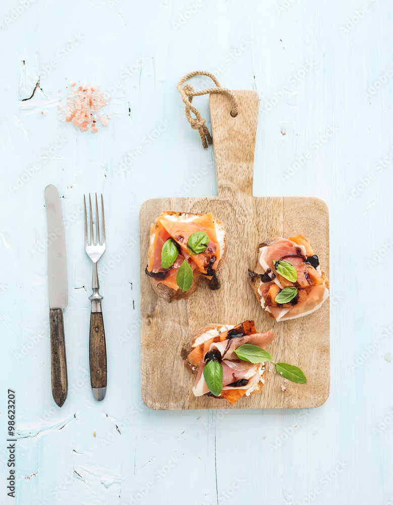 Bruschettas with Prosciutto，烤甜瓜，软奶酪和罗勒，放在木制服务板上，光线充足