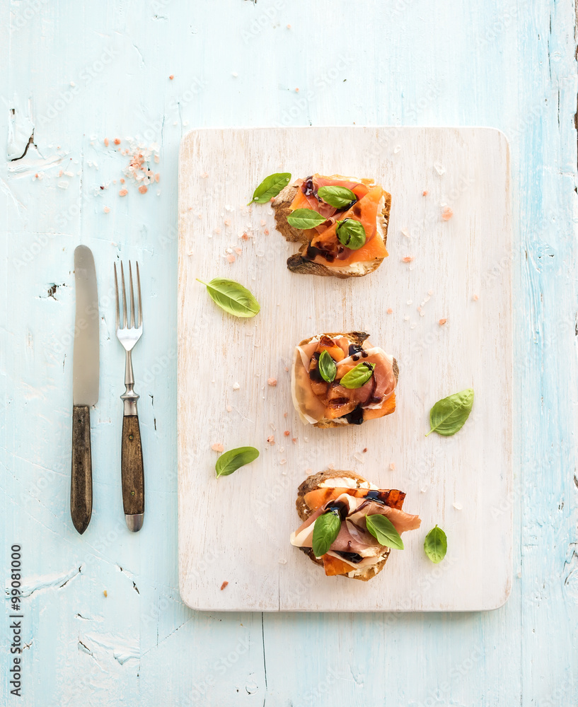 Bruschettas with Prosciutto，烤甜瓜，软奶酪和罗勒，放在木制服务板上，光线充足