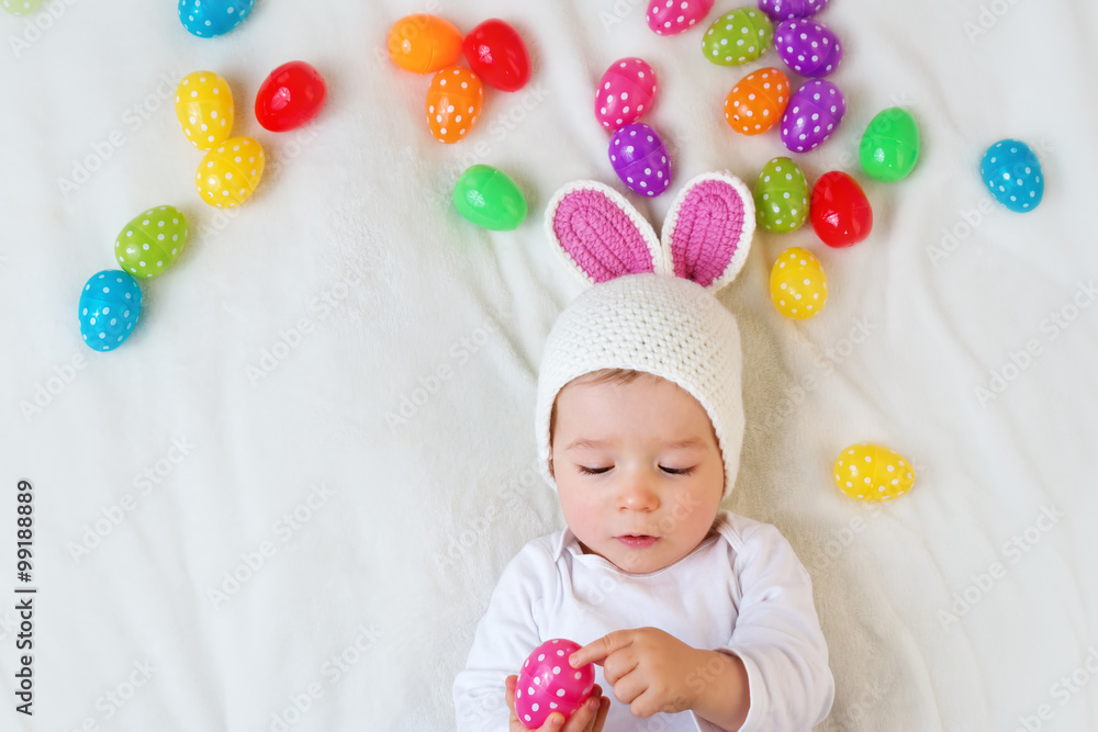 Baby boy in bunny hat lying on green blanket with easter eggs