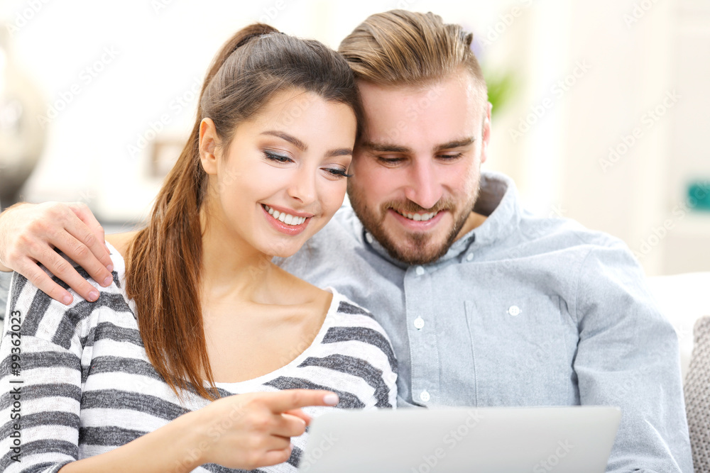 Happy couple sitting on sofa and working on a laptop