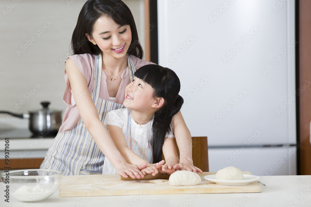 Happy mother and daughter rolling out dough