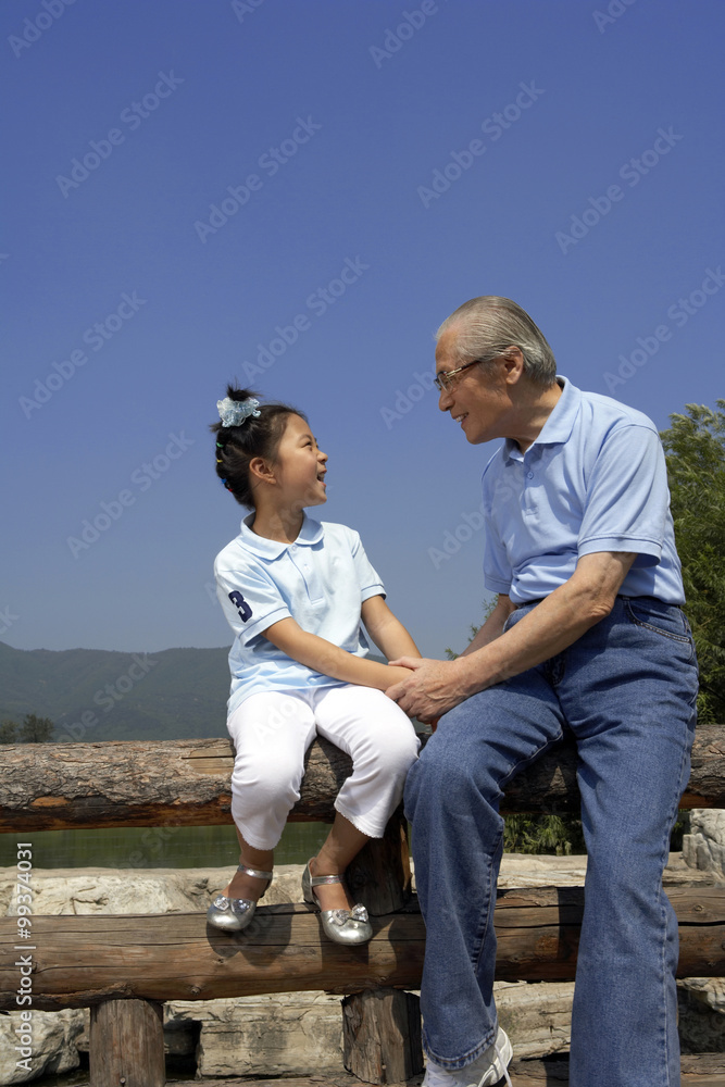 孙女和爷爷坐在栅栏上，手牵着手，看着对方