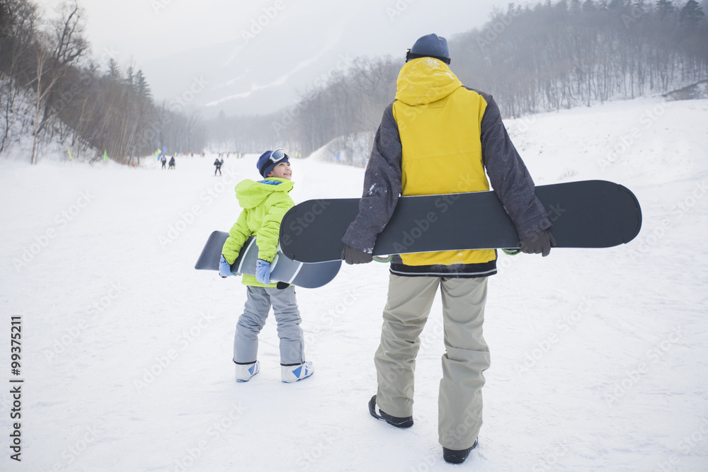 Young father and son walking with snowboards on the snow