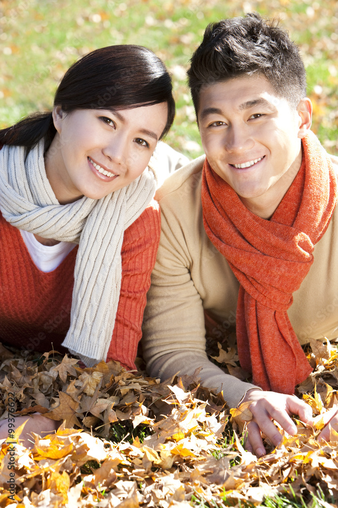 Young couple lying on the grass surrounded by Autumn leaves