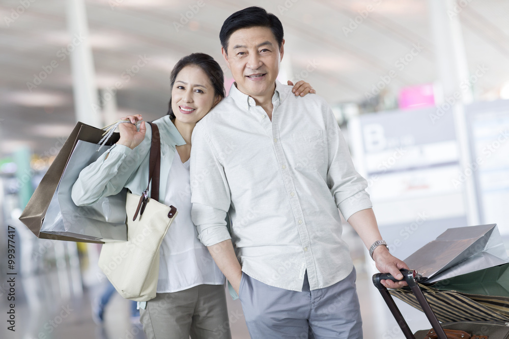 Mature couple waiting at airport with shopping bags