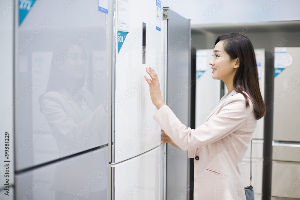 Young woman buying refrigerator in electronics store