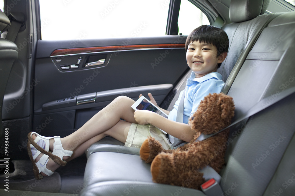 Lovely boy in car with his digital tablet and teddy bear