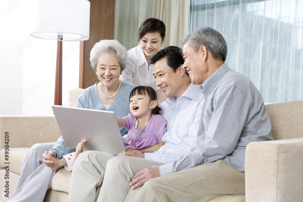 Grandparents and Parents with daughter look at Laptop on a sofa