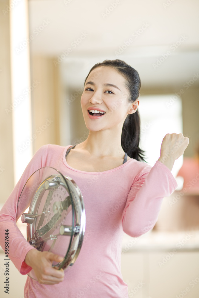 Happy young woman holding weight scale