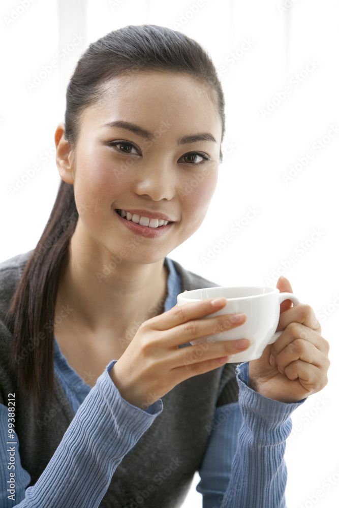 A young woman smiling while enjoying a cup of coffee