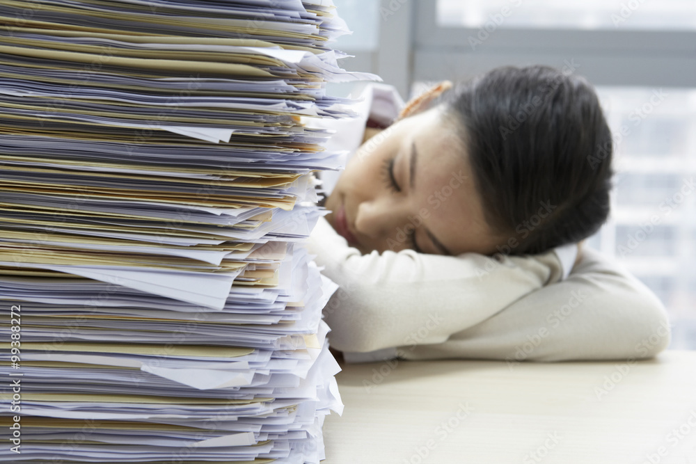 Businesswoman Sleeping Next To Pile Of Work