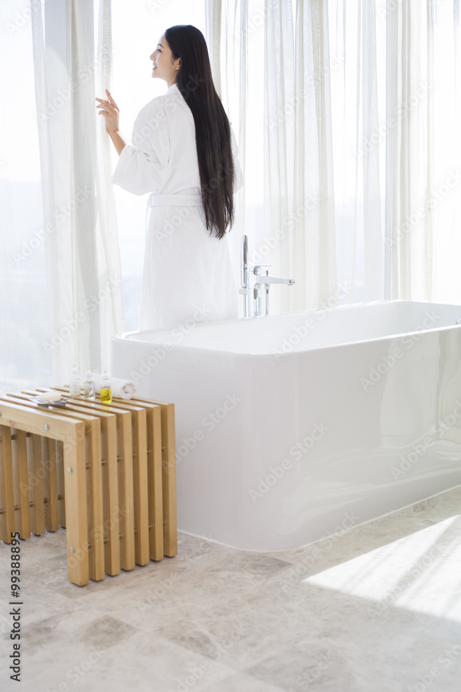 Young woman in bathrobe standing by window