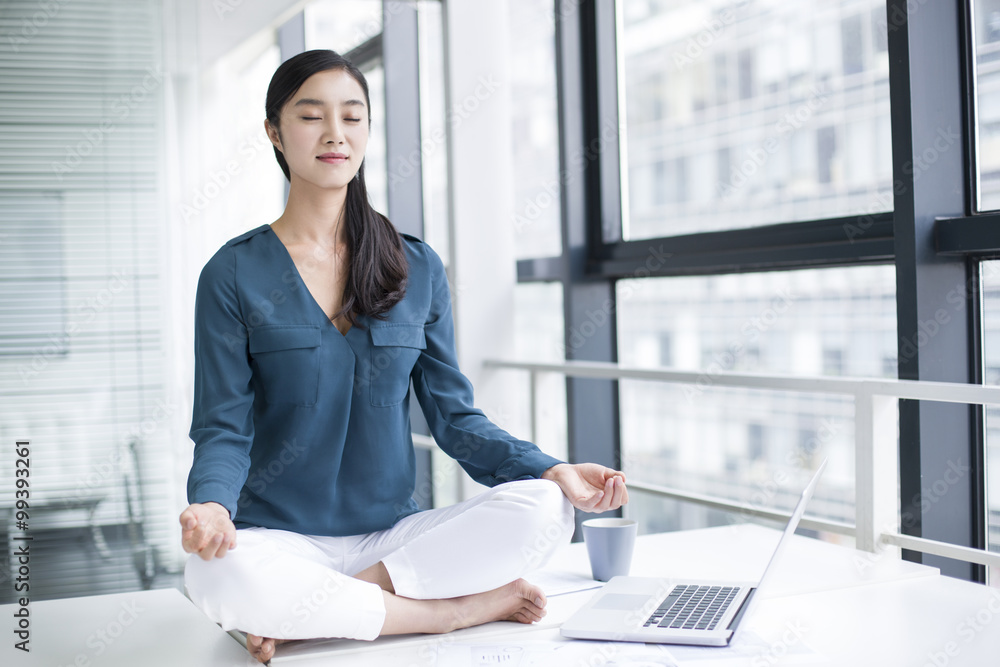 年轻女商人在办公桌上做瑜伽