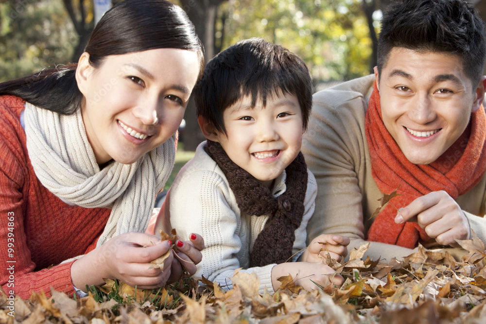 Young family lying on the grass surrounded by Autumn leaves