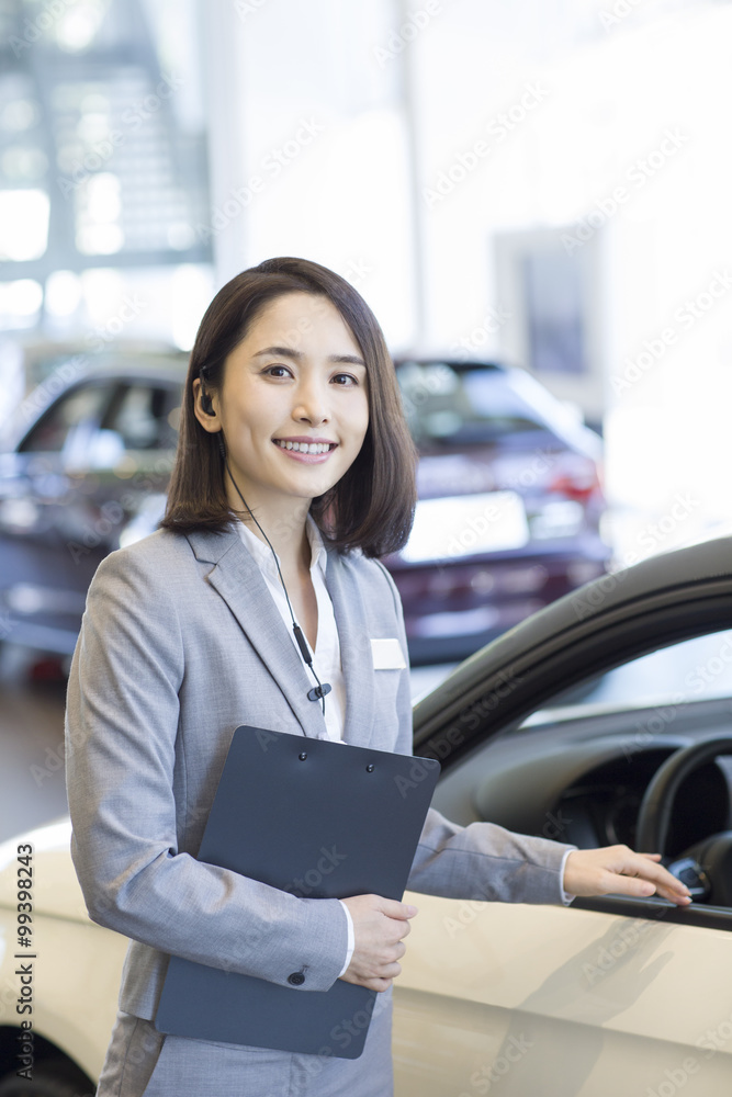 Confident saleswoman standing with new cars in showroom