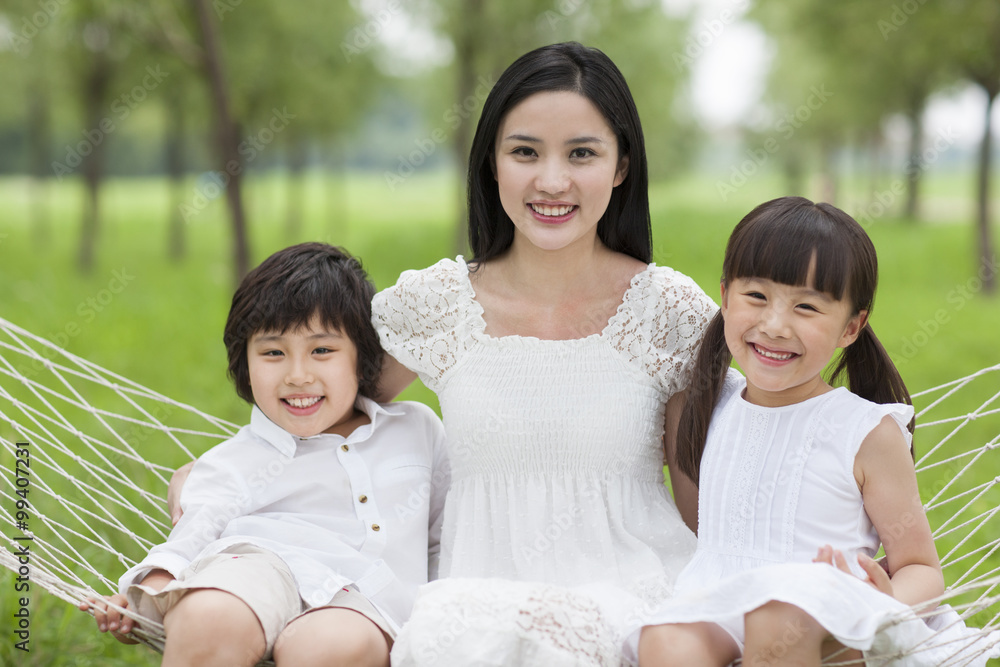 Happy young mother and kids sitting in a hammock outdoors