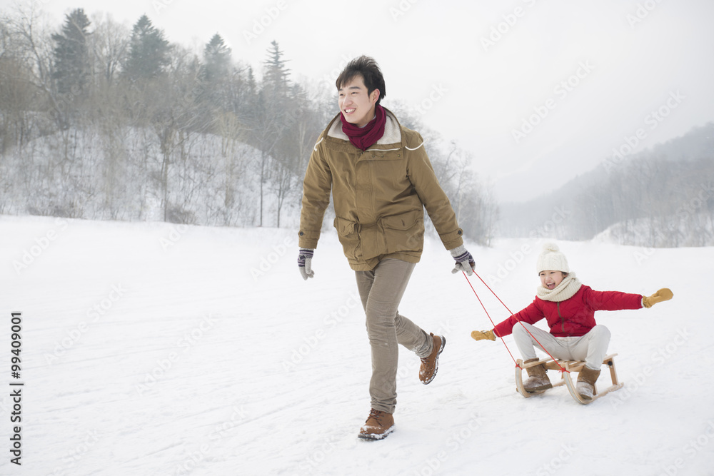 年轻父亲拉着女儿上雪橇