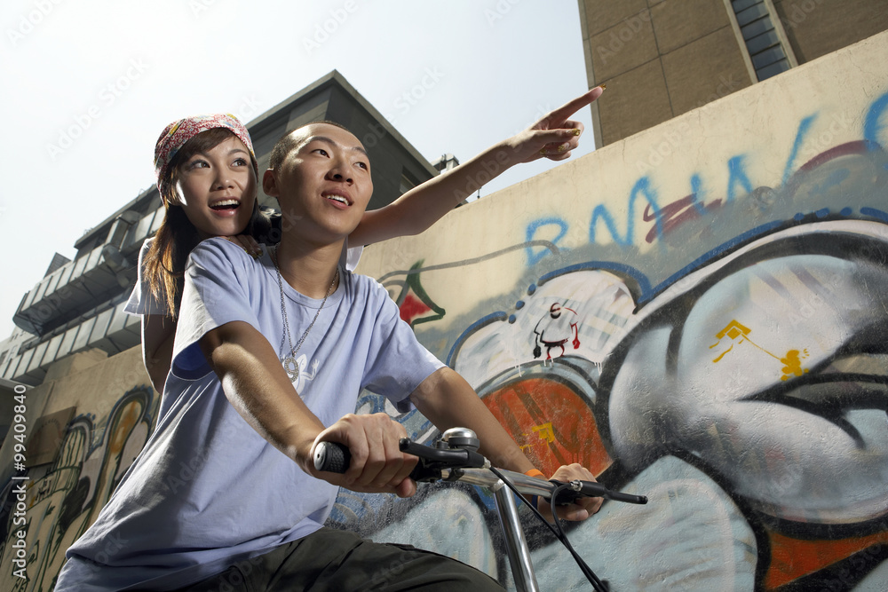 Teenage Boy And Girl On Bike In Front Of A Wall Of Graffiti