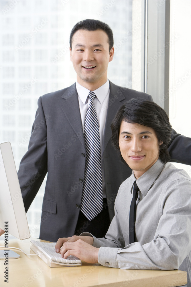 Man in business suit shows young employee something on a computer.