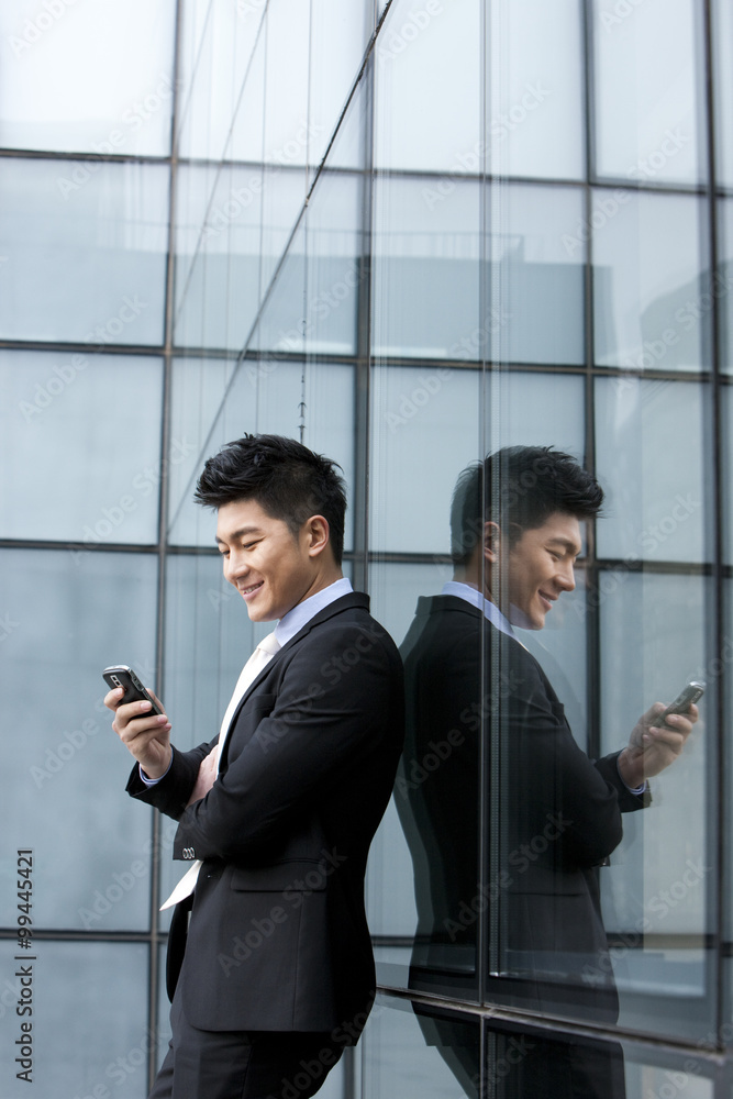 Smiling businessman with mobile phone leaning against the wall