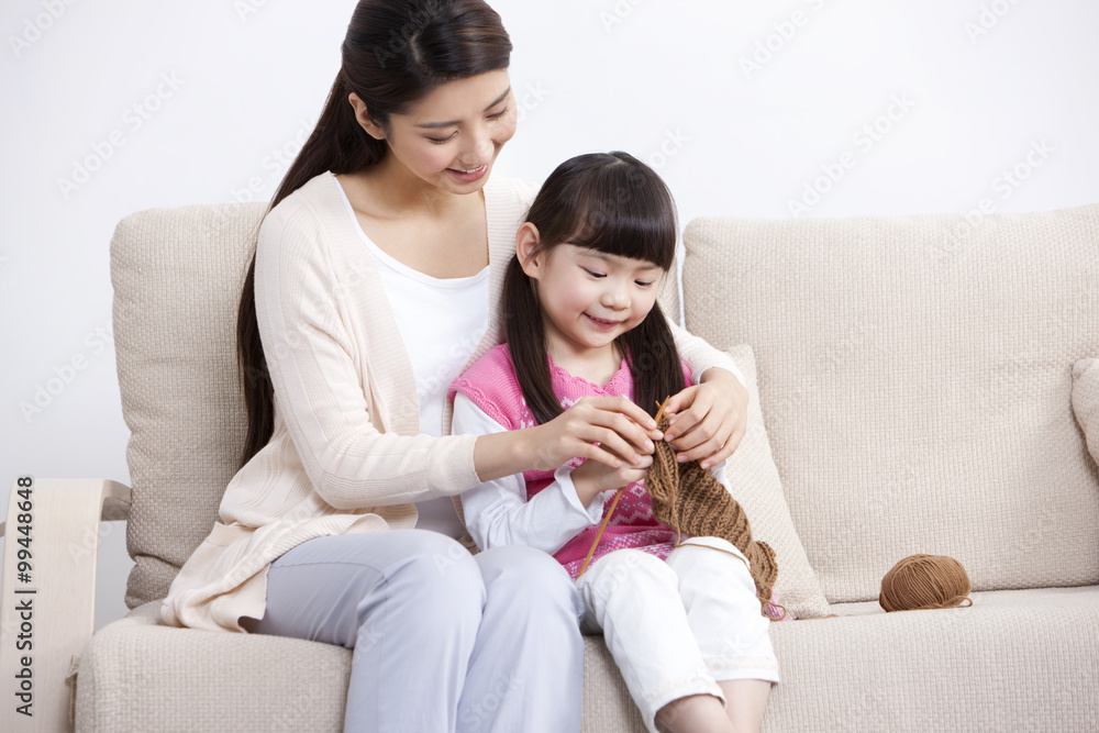 Happy mother teaching little daughter knitting at home