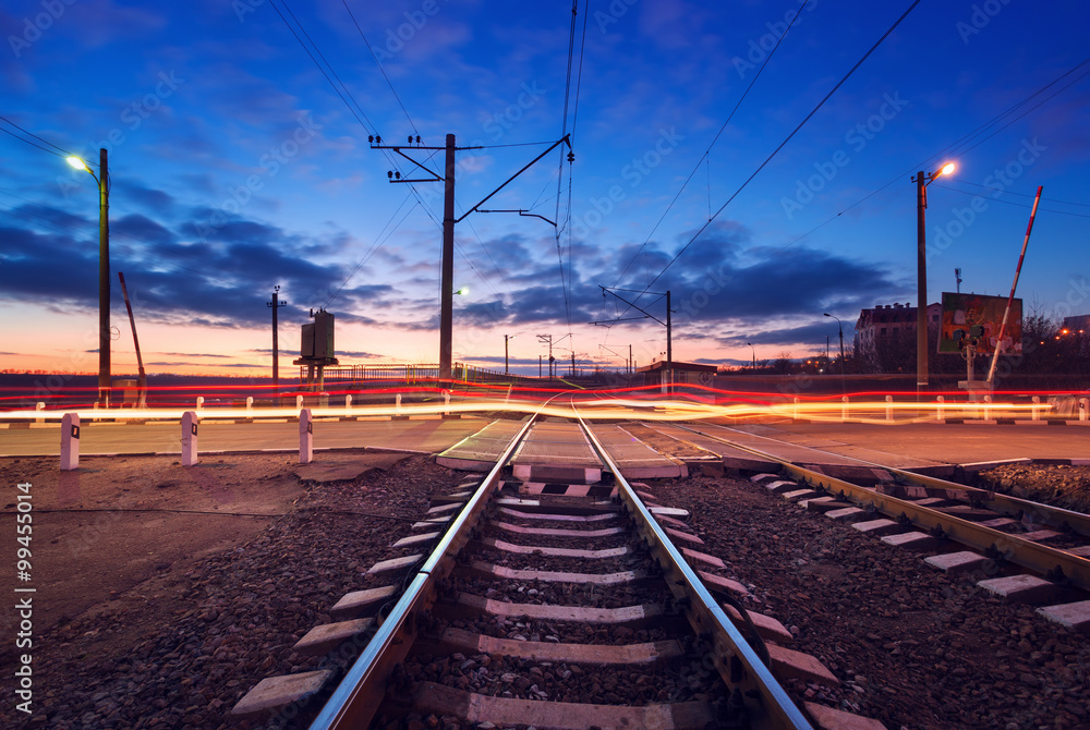 Railroad crossing with car lights in motion at night