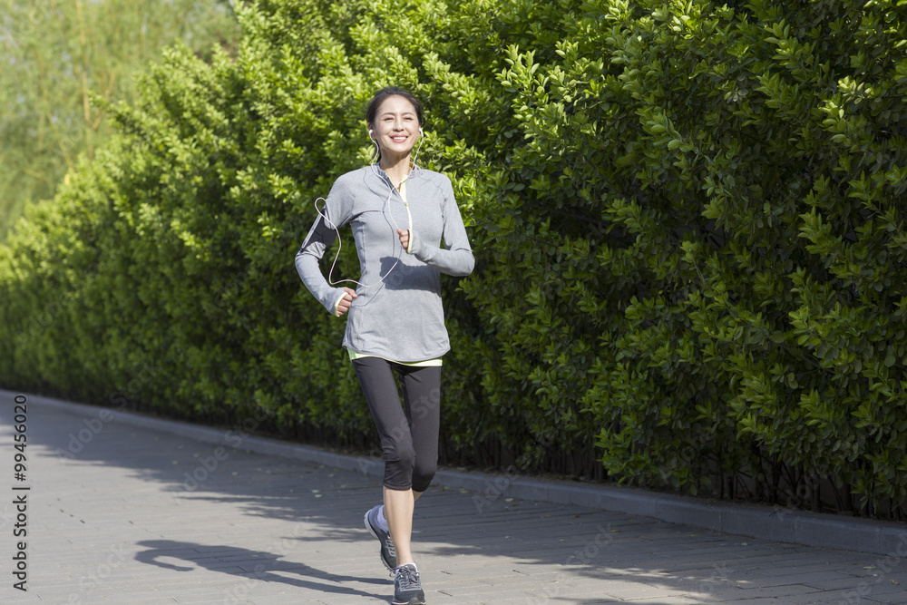 Happy mature woman running and listening to music in park