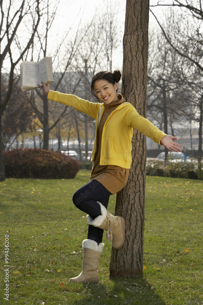 Young Woman Leaning Against A Tree Reading A Book