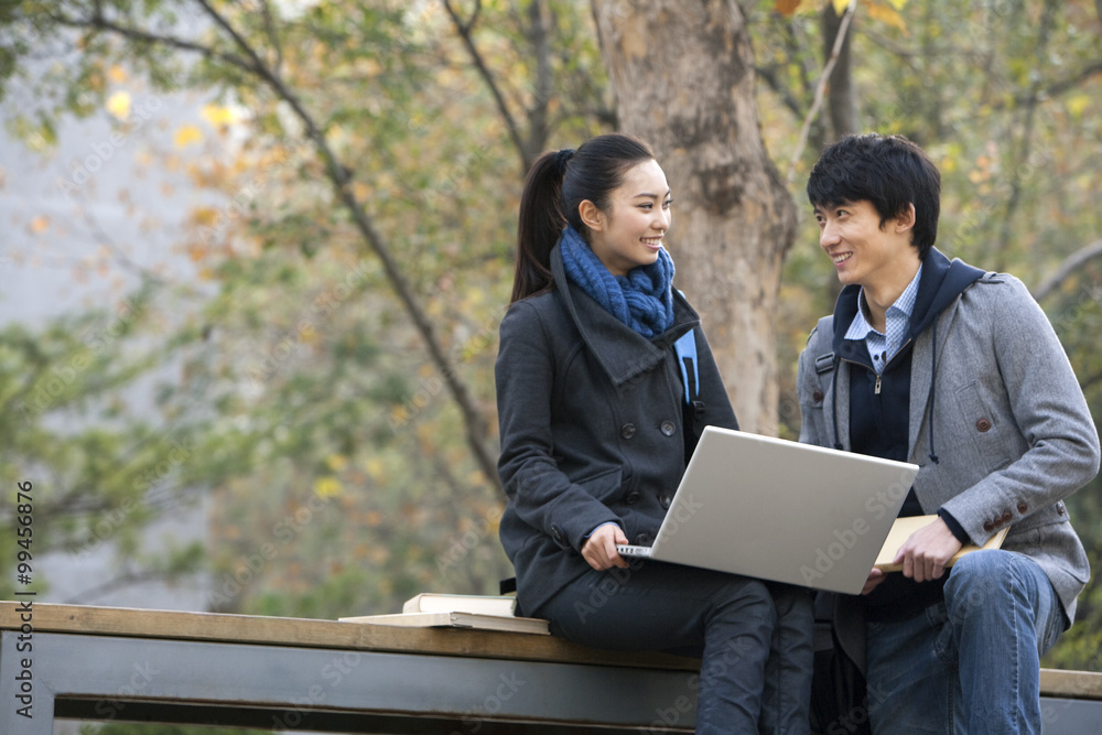 A young man and woman using a laptop together on a park bench