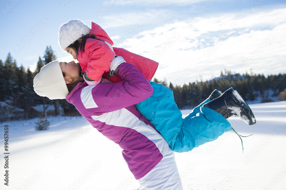 Mother holding daughter aloft on snow ground