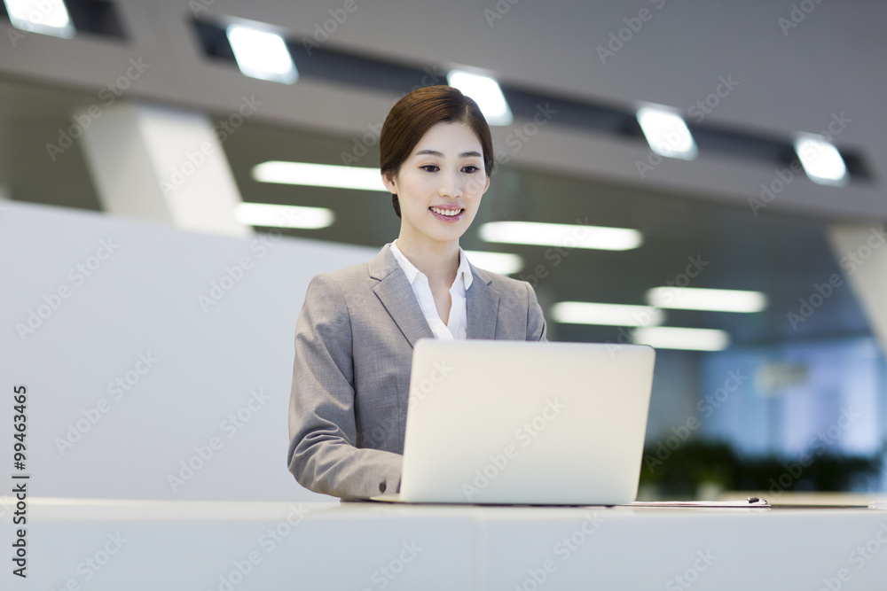 Confident receptionist using laptop at reception counter