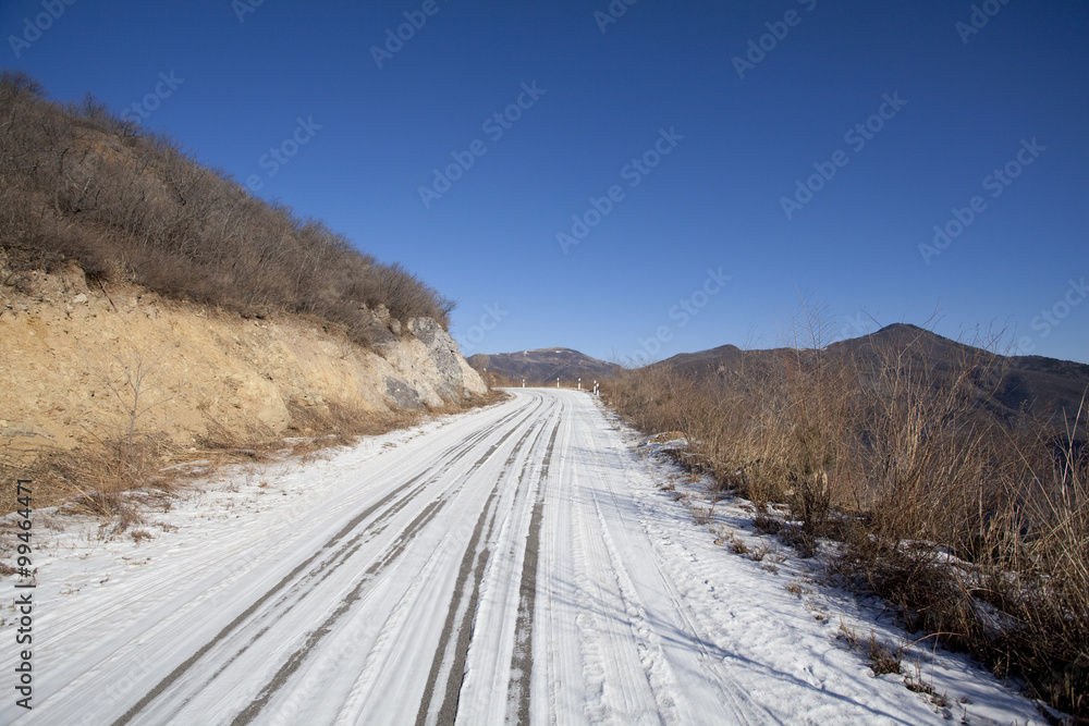 Snow-covered road going through hills in winter, Beijing China