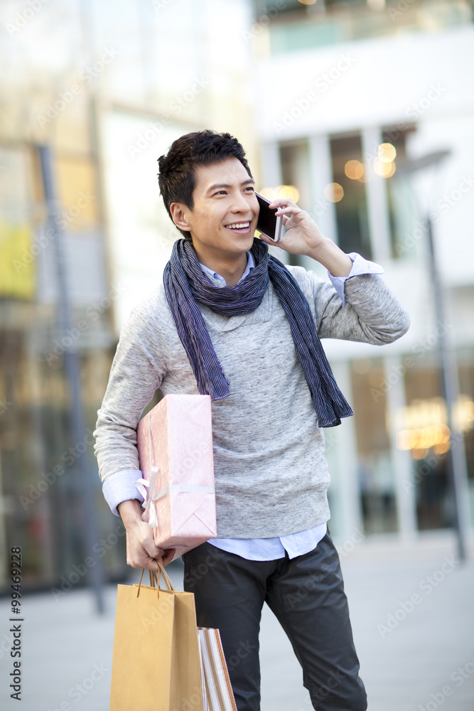 Fashionable young man with gift talking on the phone