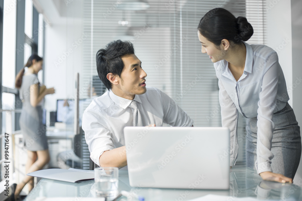 Young businesswoman and businessman talking in office