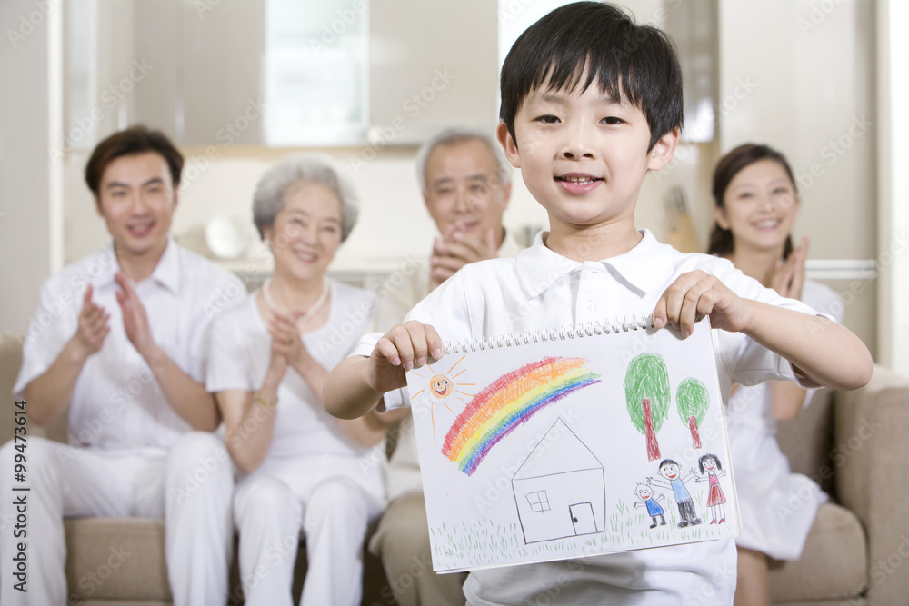 Little boy holds up a drawing in front of his family