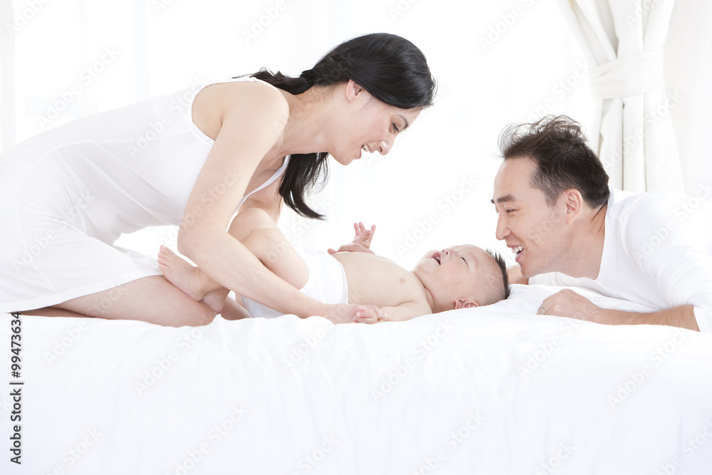 Happy young parents with cute baby in bedroom