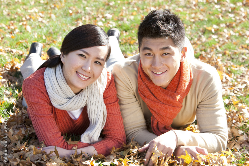 Young couple lying on the grass surrounded by Autumn leaves