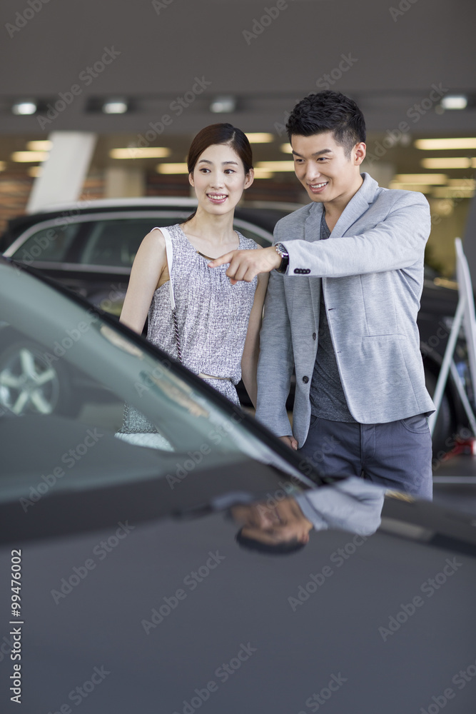 Young couple looking at new car in showroom