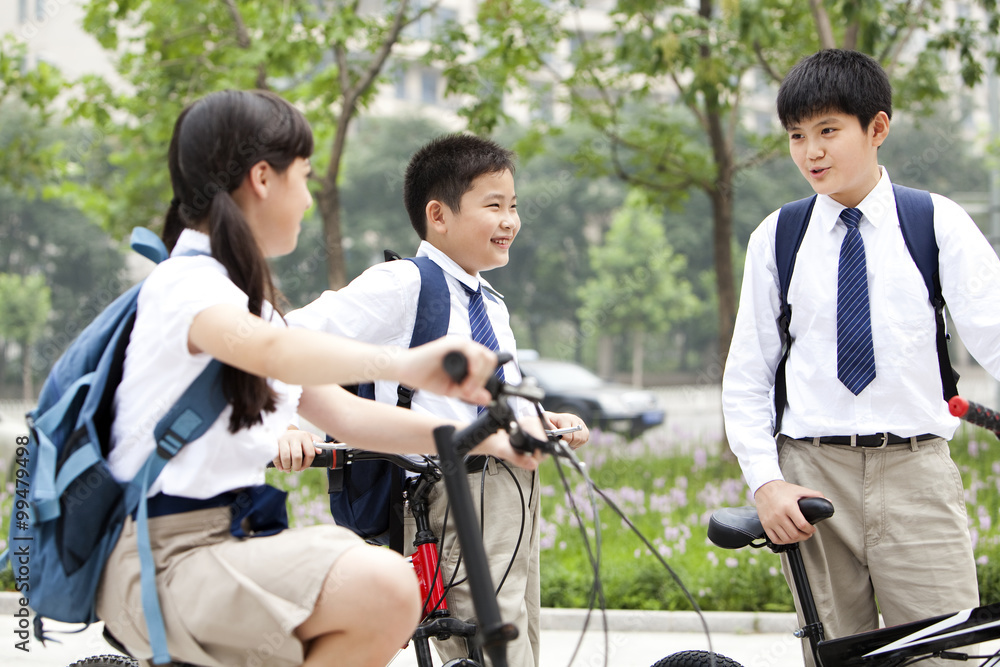 Happy schoolchildren in uniform with bicycles outdoors