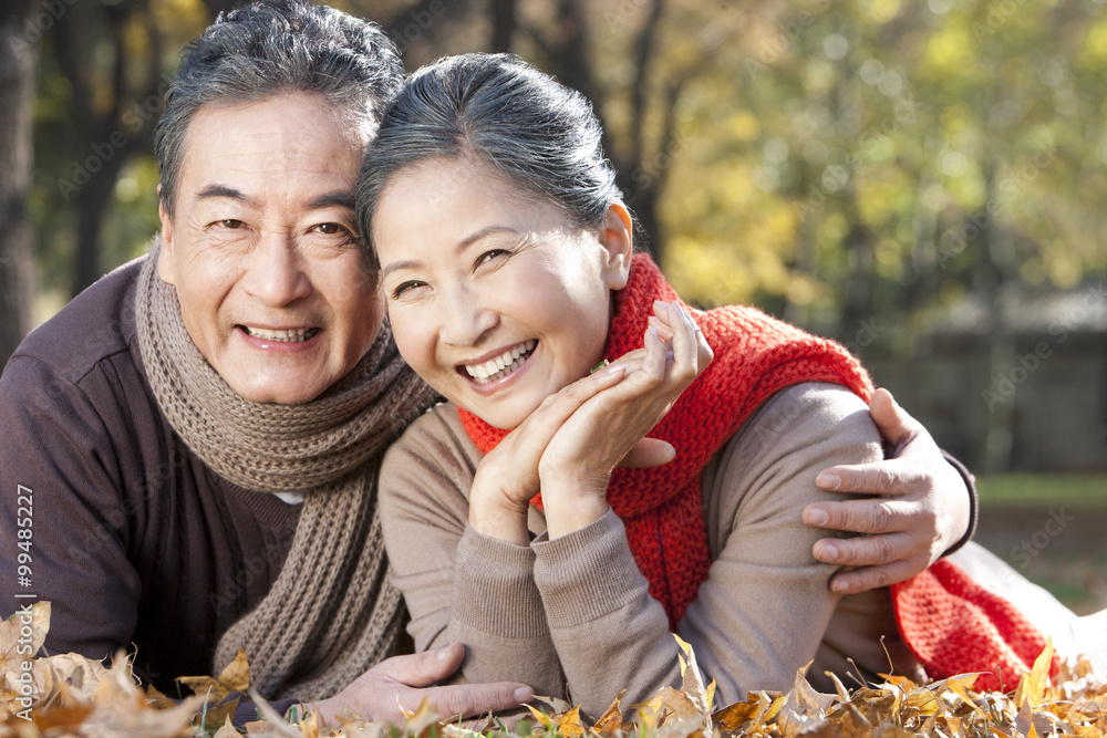 Senior couple lying on the grass surrounded by Autumn leaves